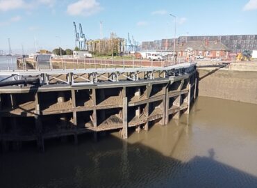 Closed flood gates at the Port of Tilbury, showing buildings and cranes in the distance.