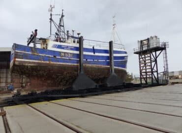 a blue and white vessel sitting in a slipway system having been winched out of the water