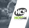Hard hats hang on a rail in an underground tunnel with rough rocky walls and a wood floor