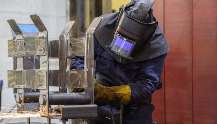 A welder wearing protective gear including a mask and making sparks fly from a metal component he is working on.