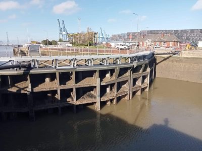 Closed flood gates at the Port of Tilbury, showing buildings and cranes in the distance.