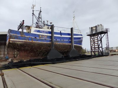 a blue and white vessel sitting in a slipway system having been winched out of the water
